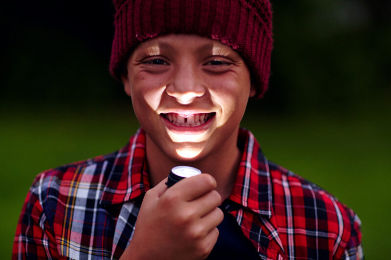 Cropped portrait of a little boy holding a flashlight under his chin