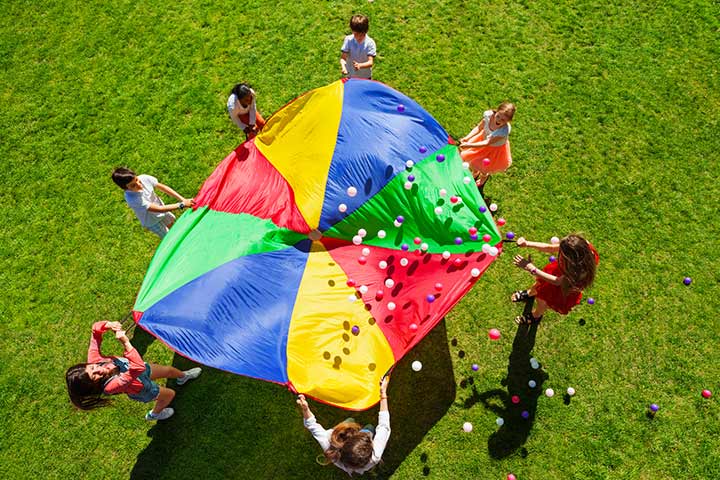 Students stand around a large parachute with small balls bouncing on the top of it.