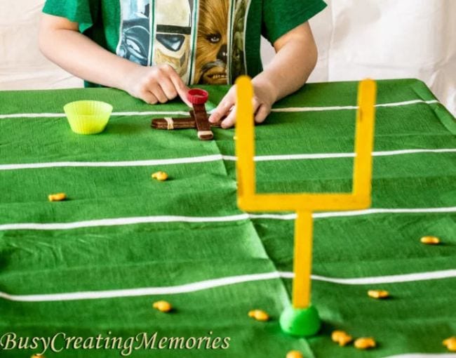 Child using a catapult made of wood craft sticks to launch goldfish crackers through miniature goal posts (Football Activities)