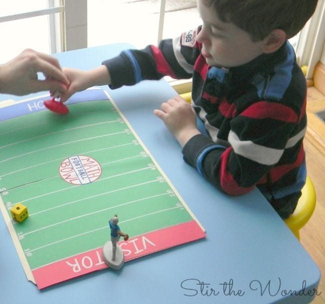 Child moving a plastic football player figurine down a paper football field (Football Activities)