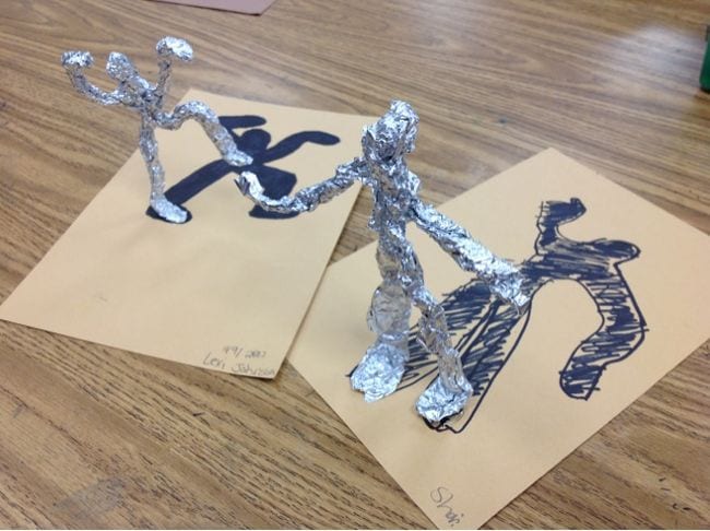 Two figures sculpted from aluminum foil, with their shadows drawn below