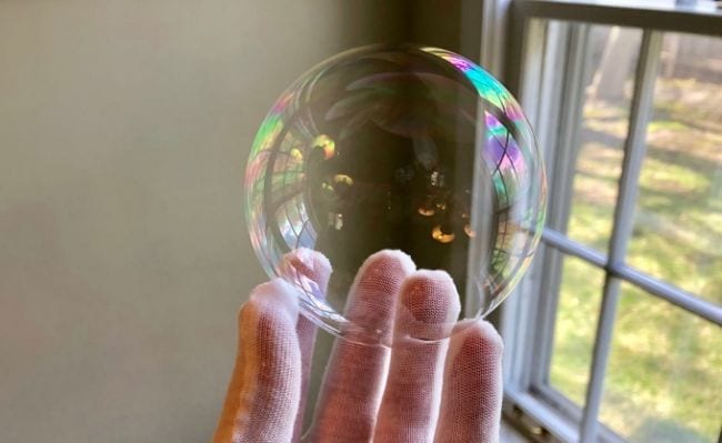 Student's gloved hand holding a soap bubble next to a window (Fourth Grade Science)