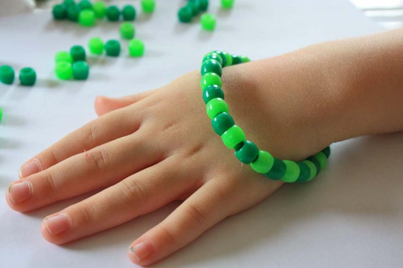 A child's hand is shown wearing a bracelet that has been constructed from pipe cleaners and different shades of green beads (St. Patrick's Day crafts for kids)