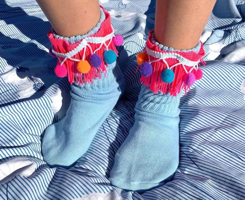 Light blue socks decorated around the band with pink fringe and a garland of pompoms