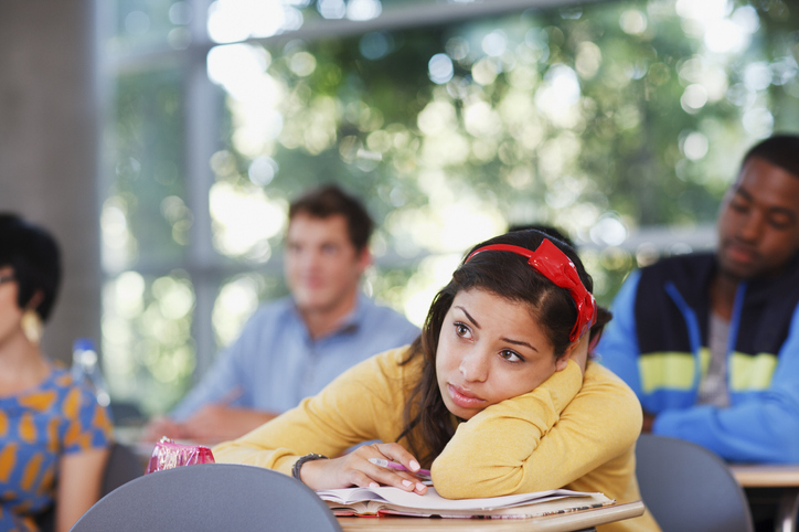 A girl is in a classroom with her head in her hands looking mildly frustrated.