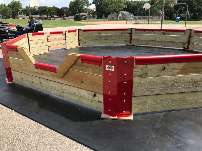A wooden gaga ball pit with red brackets on a black rubber surface