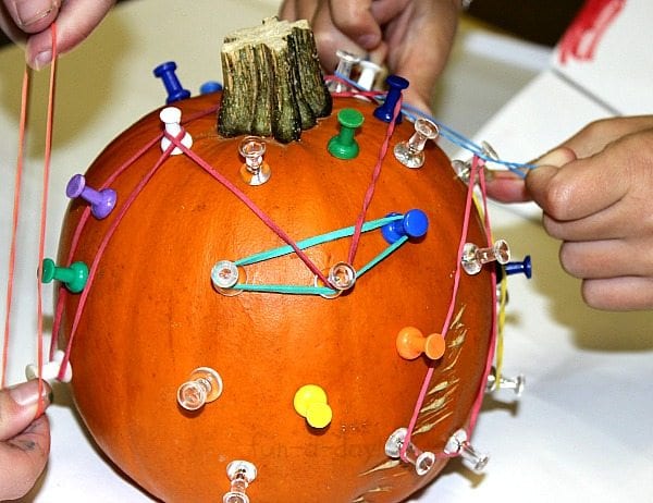 a small pumpkin with push pins stuck into it, with rubber bands stretched between the pins