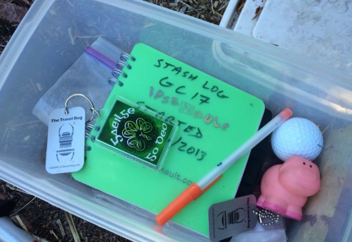 The contents of a geocaching box, including logbook, pen, travel bug tag, and small toys