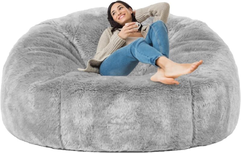 A woman lounges on a huge gray fur bean bag chair.