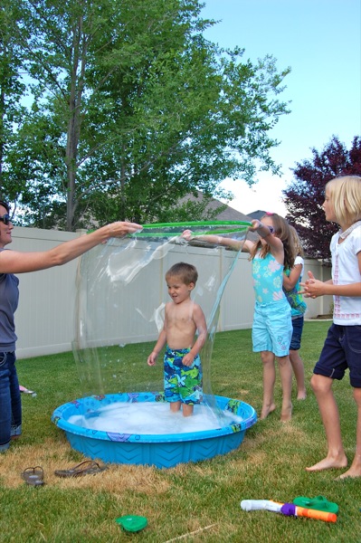 A child is seen standing inside a kiddie pool while a giant bubble surrounds him.