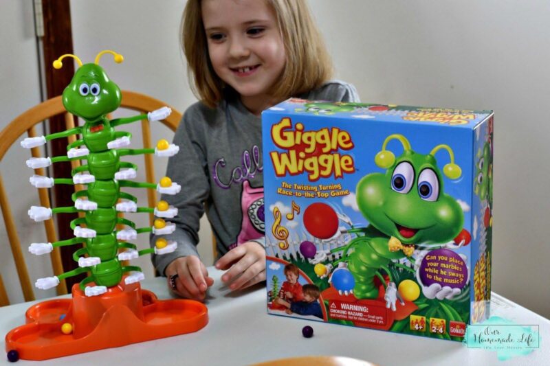 A little girl sits in front of a game box and a caterpillar tower that has many arms that are holding marbles in this example of marble games.