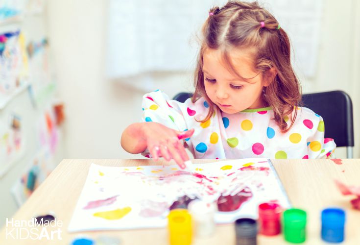 A little girl sits quietly at a table, finger painting