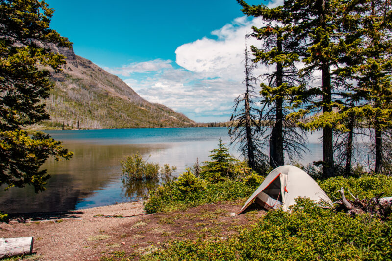 Photograph of a tent alongside a mountain lake on a mostly clear day in Glacier National Park, as an example of best family vacations