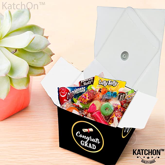 Graduation cap treat box filled with assorted candy on a table next to a small plant, as an example of senior graduation gifts