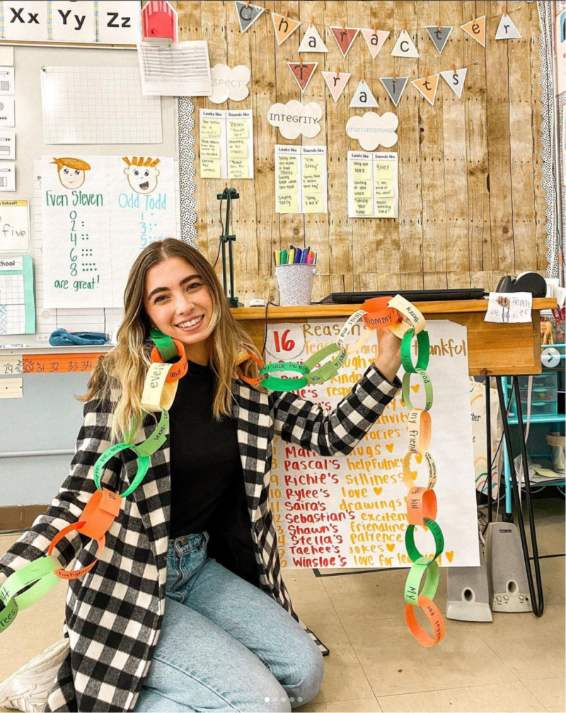 Teacher sitting on the floor of classroom holding a paper gratitude chain.