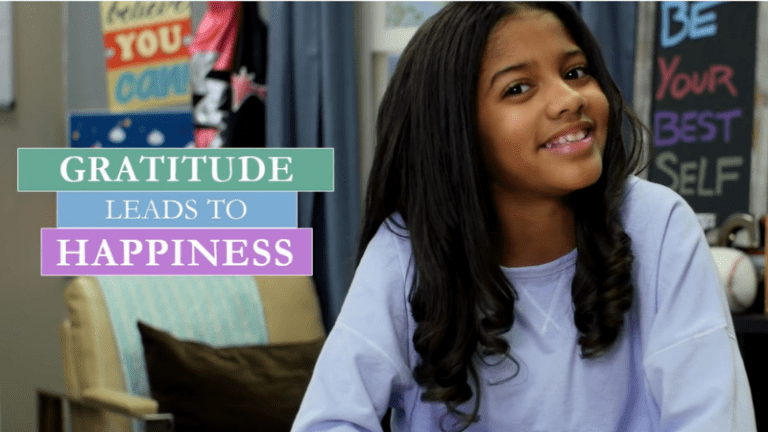 Screenshot from gratitude videos: Young girl smiling in a classroom; "Gratitude leads to happiness"
