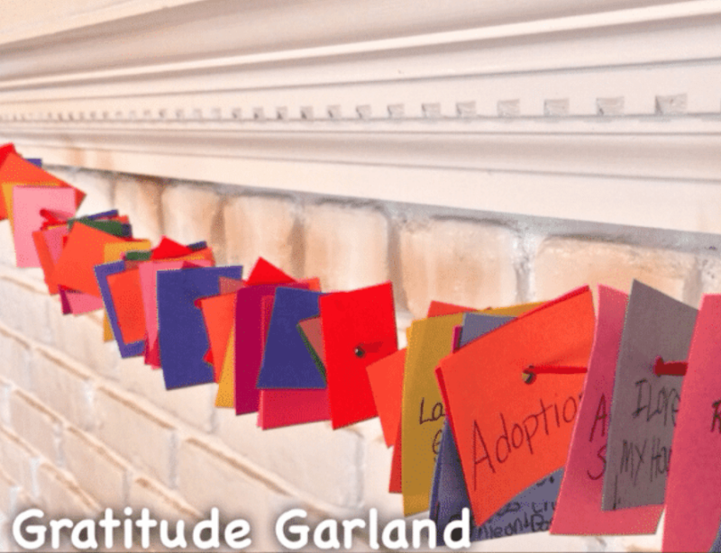 Gratitude activities for kids include a garland made of small squares with expressions of gratitude on them are strung together on a string and hung on a mantle.
