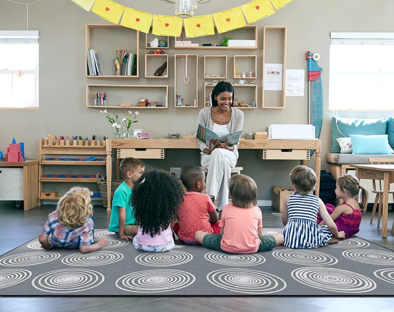 Teacher reading to a classroom of children sitting on a grey rug.