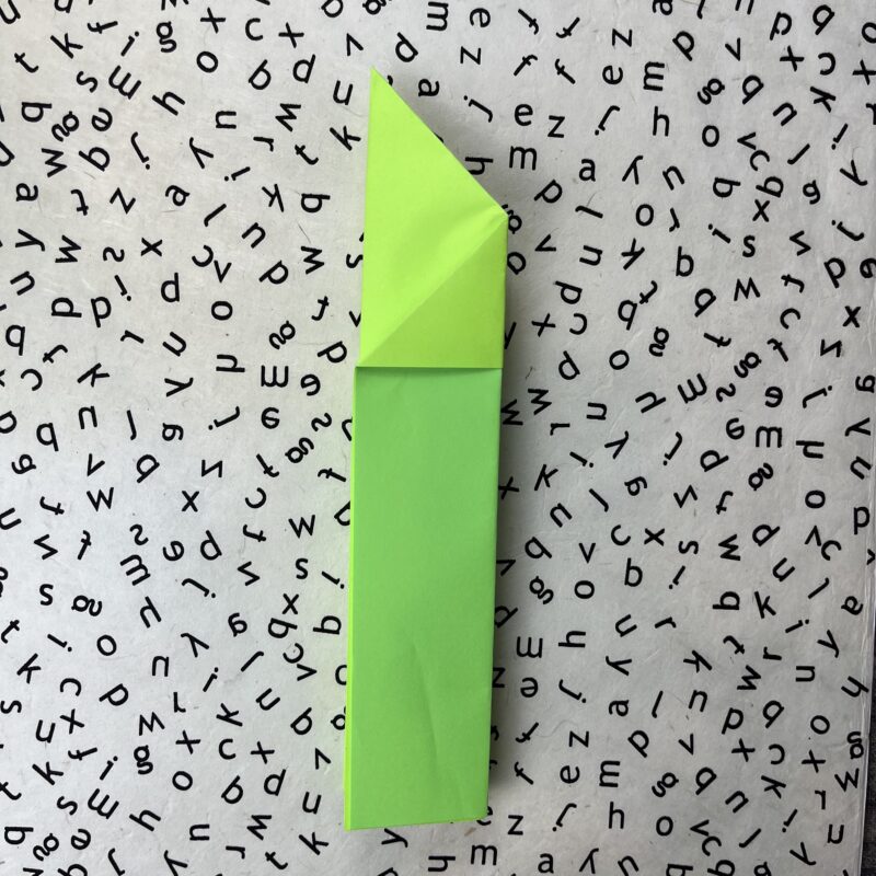 Step 5 of how to make a paper airplane. Green plane fully folded.