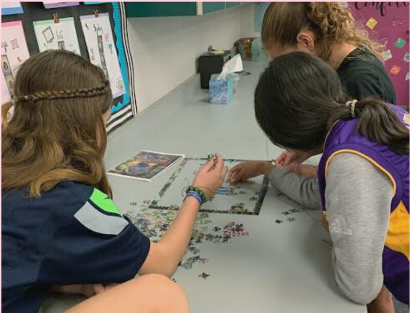 Middle school students putting a puzzle together on a table as an example of team building activities for kids. 