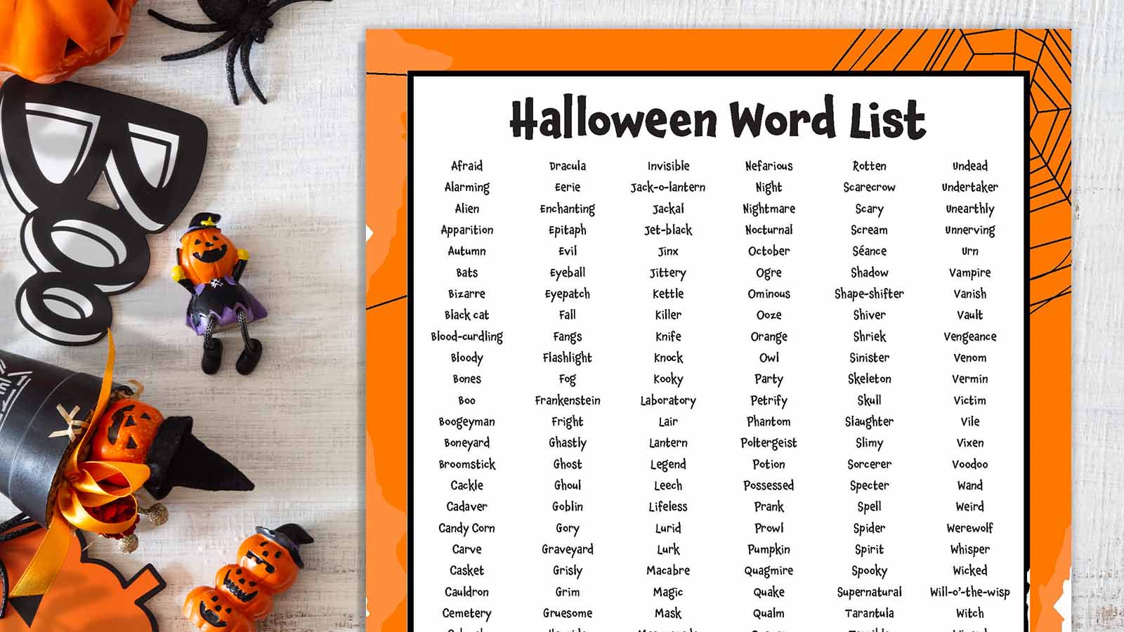 Printable Halloween word list on with Halloween decorations scattered beside it.