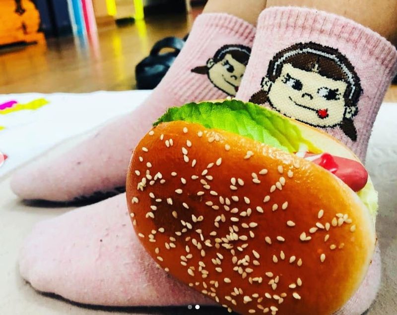 Pink socks with a face licking its lips, and a toy hamburger attached
