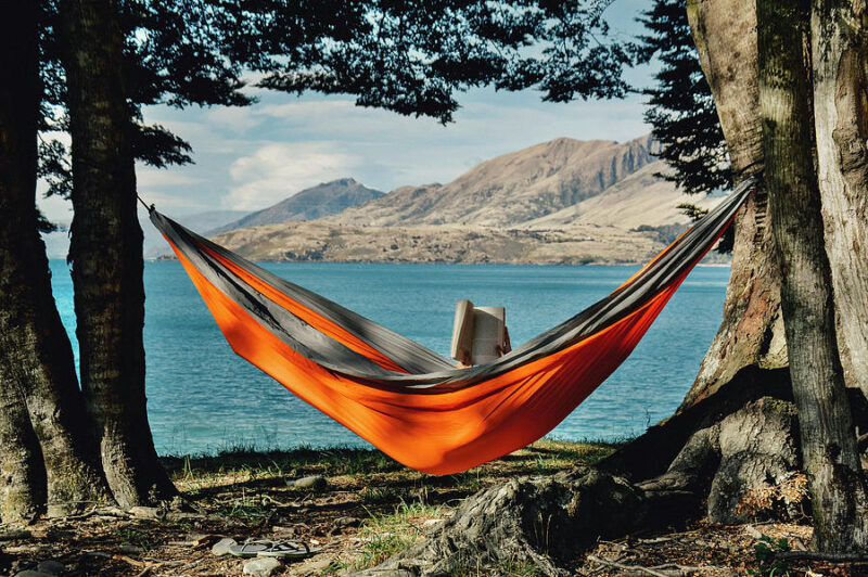 Person reading in hammock with mountains and lake in background.