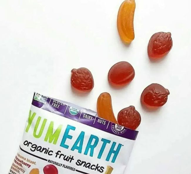 Open bag of YumEarth fruit snacks with fruit-shaped gummies spread on a white table