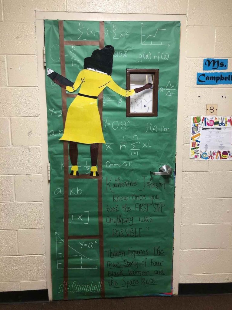 A door is decorated with a green background to look like a chalkboard. A woman is shown from behind on a ladder writing math equations on the chalkboard.