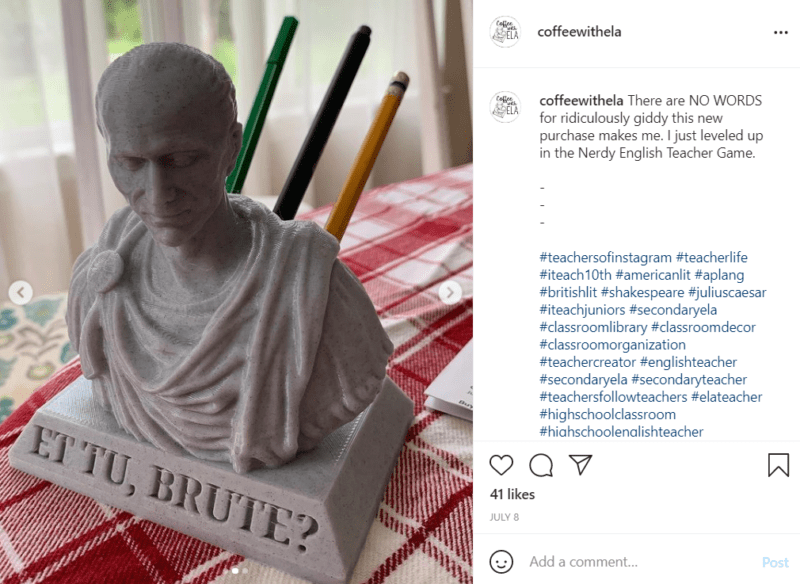 A grey bust of Julius Caesar sits on a table with a gingham tablecloth. The phrase "Et Tu, Brute?" is on the bust and pencils and pens are able to be stored in the back of the bust to replicate the Roman emperor being stabbed in the back, , as an example of high school classroom decorations