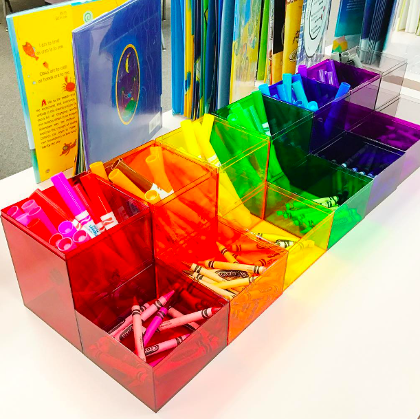 Rainbow hued plastic bins holding crayons and markers