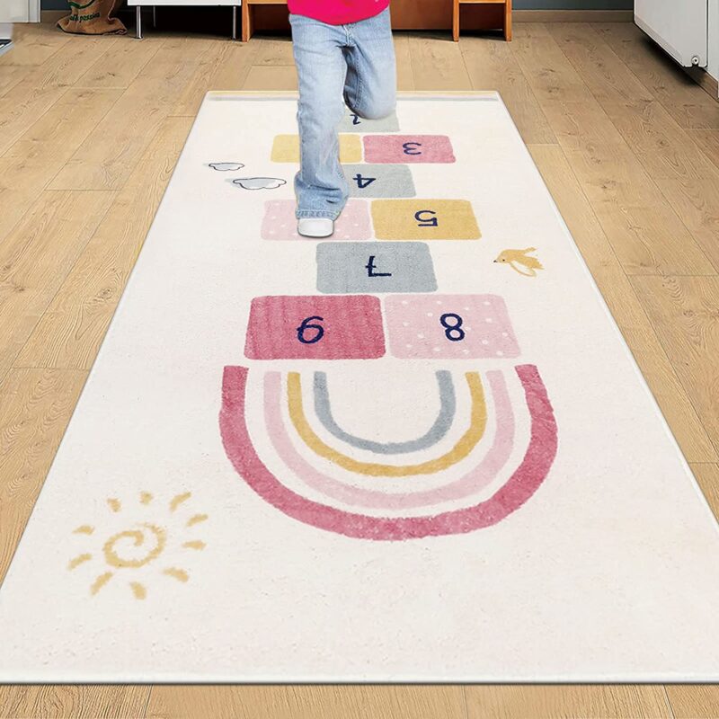 A child is shown from the waist down playing on a hopscotch rug that also has a rainbow on it.