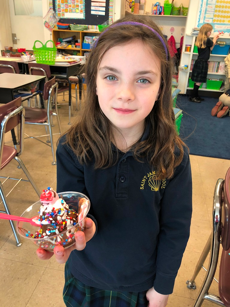 A little girl is shown holding a sculpture of an ice cream sundae 