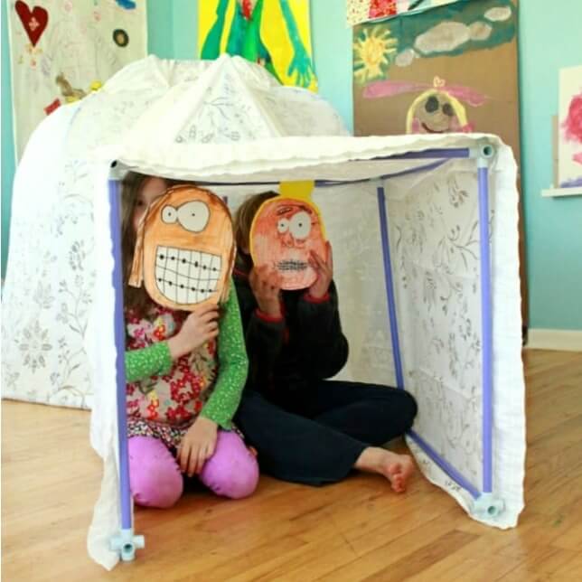 two kids in an igloo made with a sheet and building rods for a fun winter activity