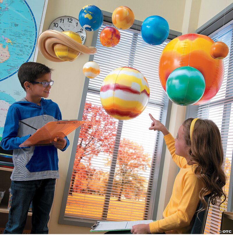 Two students with clipboards pointing to inflatable solar system in classroom