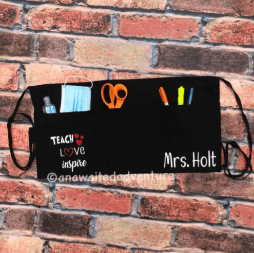A black apron has various school items in it like scissors and pens.