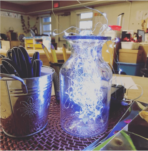 A jar in a classroom has fairy lights in it.