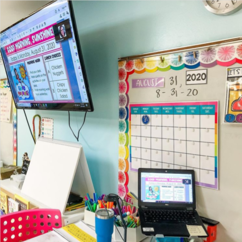 A screen is projecting a chart in a classroom that says Good Morning Sunshine! and includes the weather and chores.