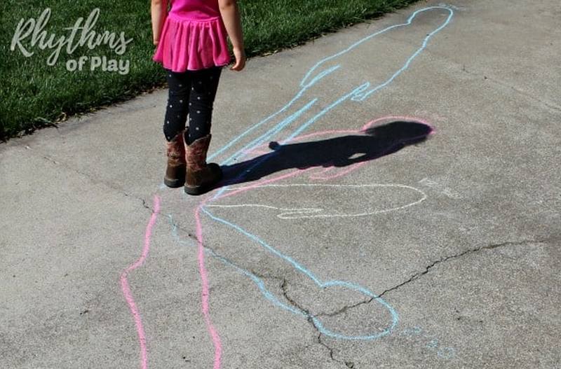 Student comparing their shadow to a number of chalk outlines on the sidewalk as part of a science experiment