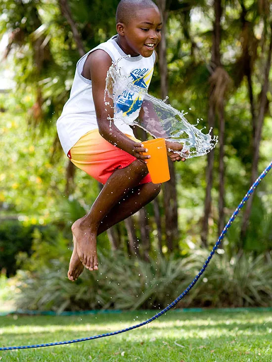 Summer camp activities include toys like jump ropes as seen here. A boy jumps over a jump rope while holding a cup of water. 