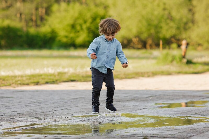 Toddler jumping in a puddle outside.