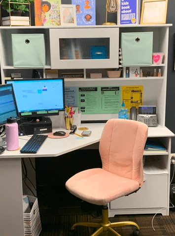 a principal's work area with white desk and bookcase and a pink rolling office chair