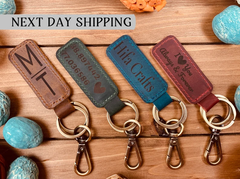 Several leather keychains in different colors are shown with different things inscribed on them. 