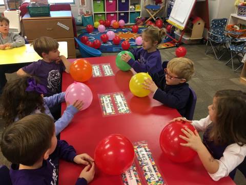 kids sitting at their desks in a classroom, each with a balloon in front of them, as an example of team-building games and activities
