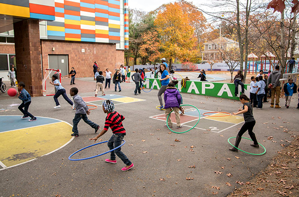 Kids are shown on a school blacktop playing with hula hoops.