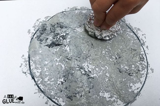 Child's hand using foil ball dipped in paint to create a moon painting