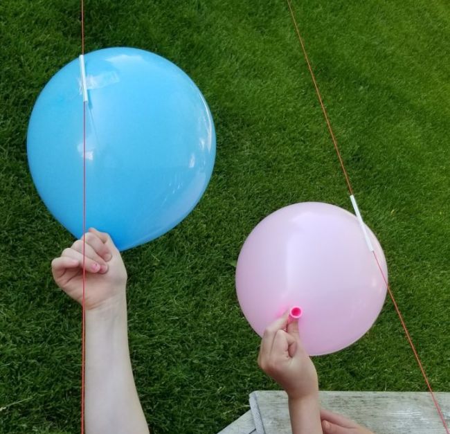 Students holding the ends of balloons taped to drinking straws on a string
