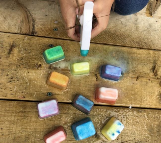 Child's hands holding a spray bottle over colorful ice cubes on a wood surface