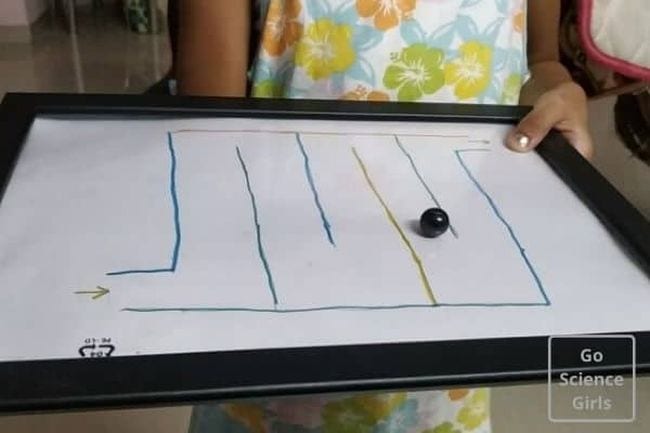 Child using a magnet to move a metal marble through a paper maze