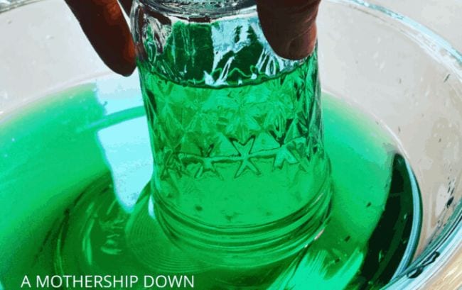 Student's hand lifting an upside-down jar from a bowl of green water, with water kept inside the jar by air pressure